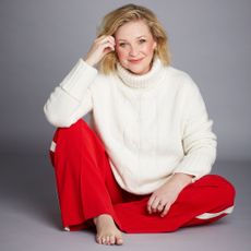 Joanna Page in a red outfit posing against a plain grey background