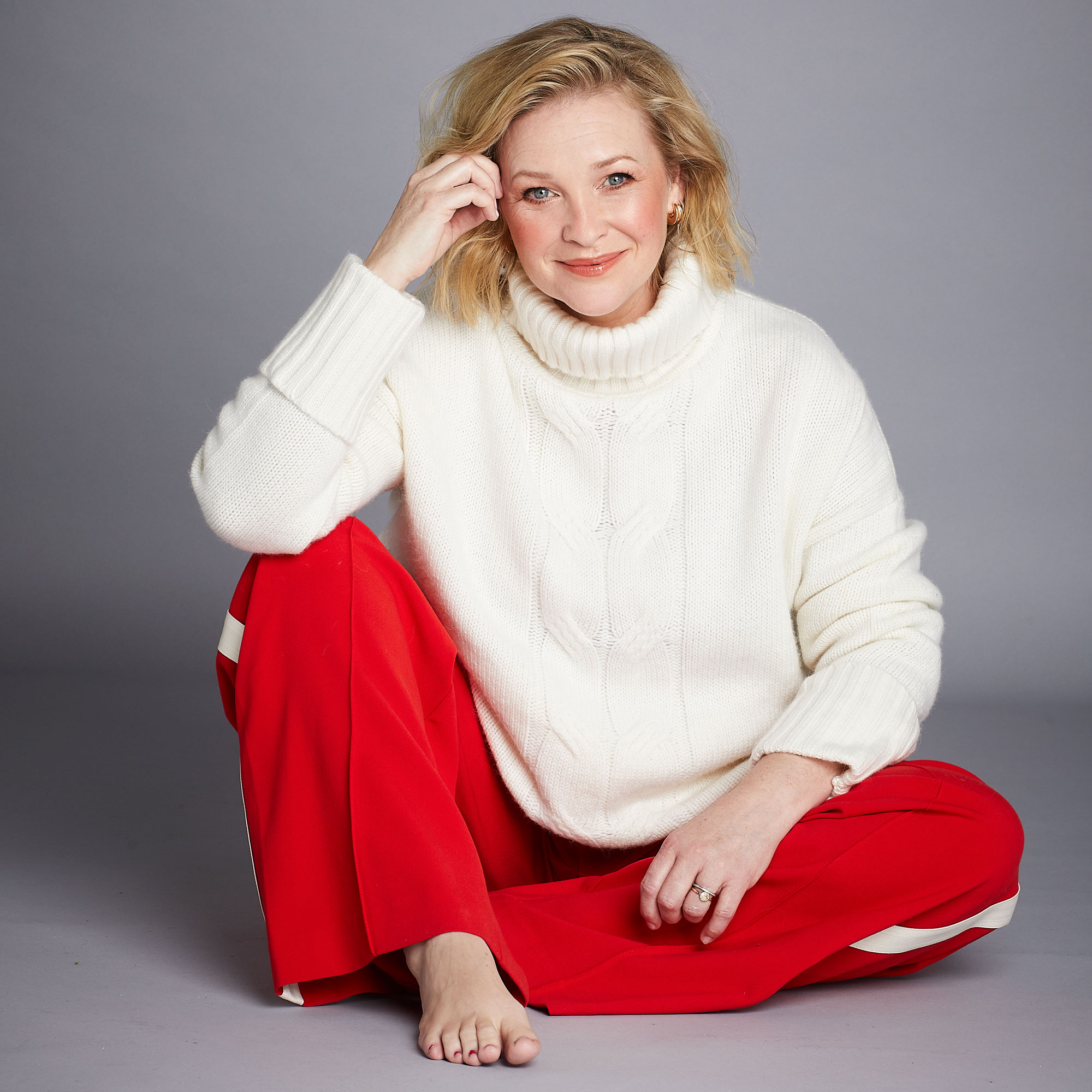 Joanna Page in a red outfit posing against a plain grey background
