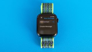 Detail shot of an Apple Watch SE on a bright blue background showing the steps to set up and send a Check In notification in watchOS 11 