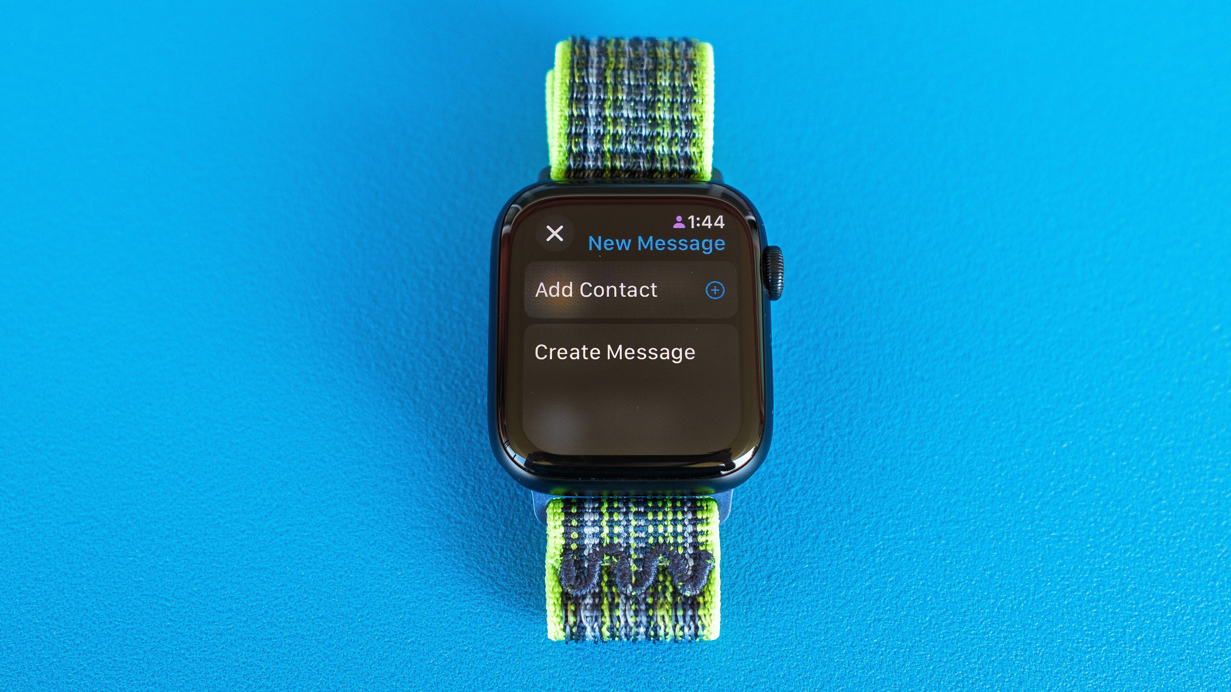 Detail shot of an Apple Watch SE on a bright blue background showing the steps to set up and send a Check In notification in watchOS 11 