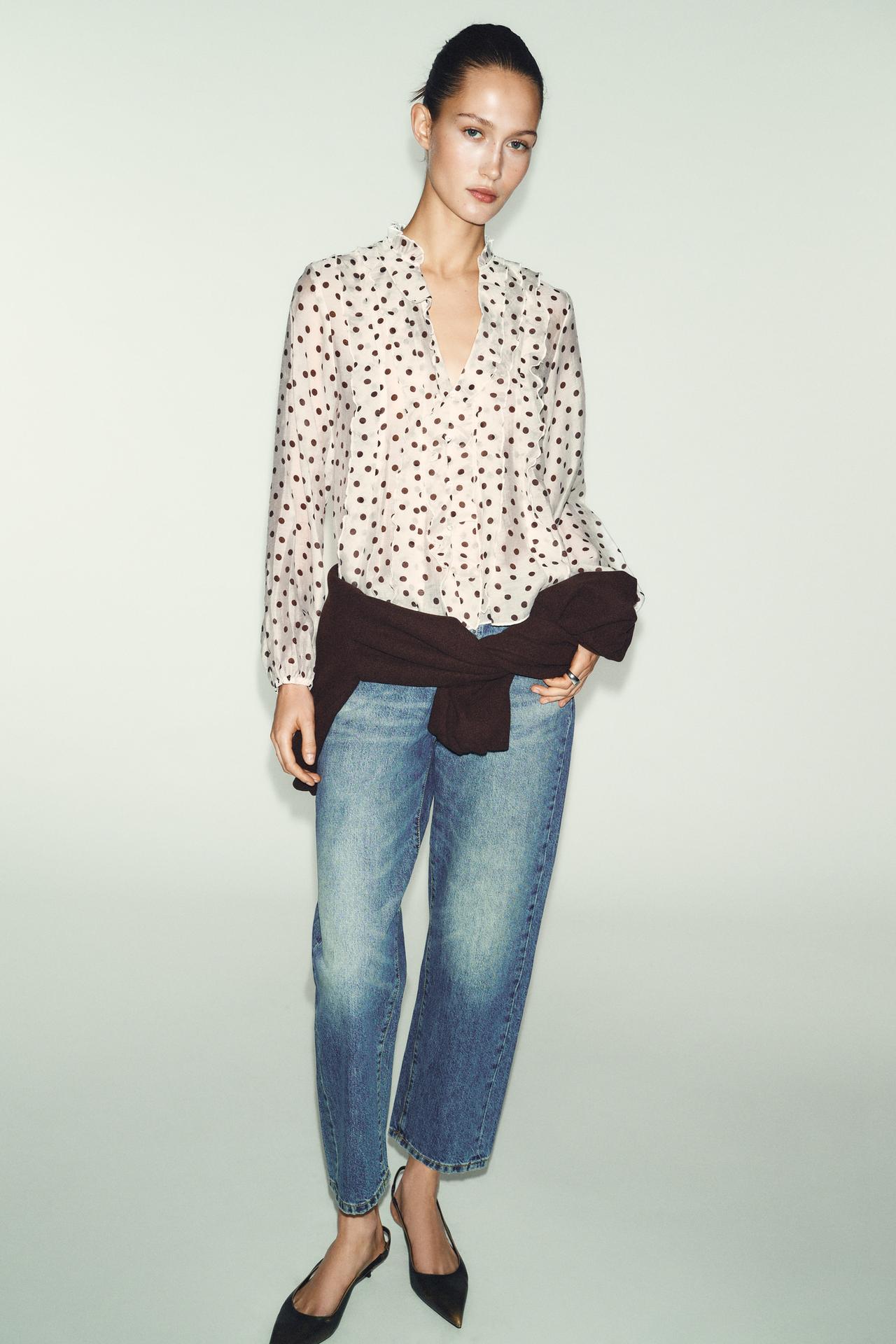 Model is wearing long sleeve brown polka dot top with medium wash straight leg jeans and a pointed toe sling back kitten heel. She also has a sweater tied around her waist.
