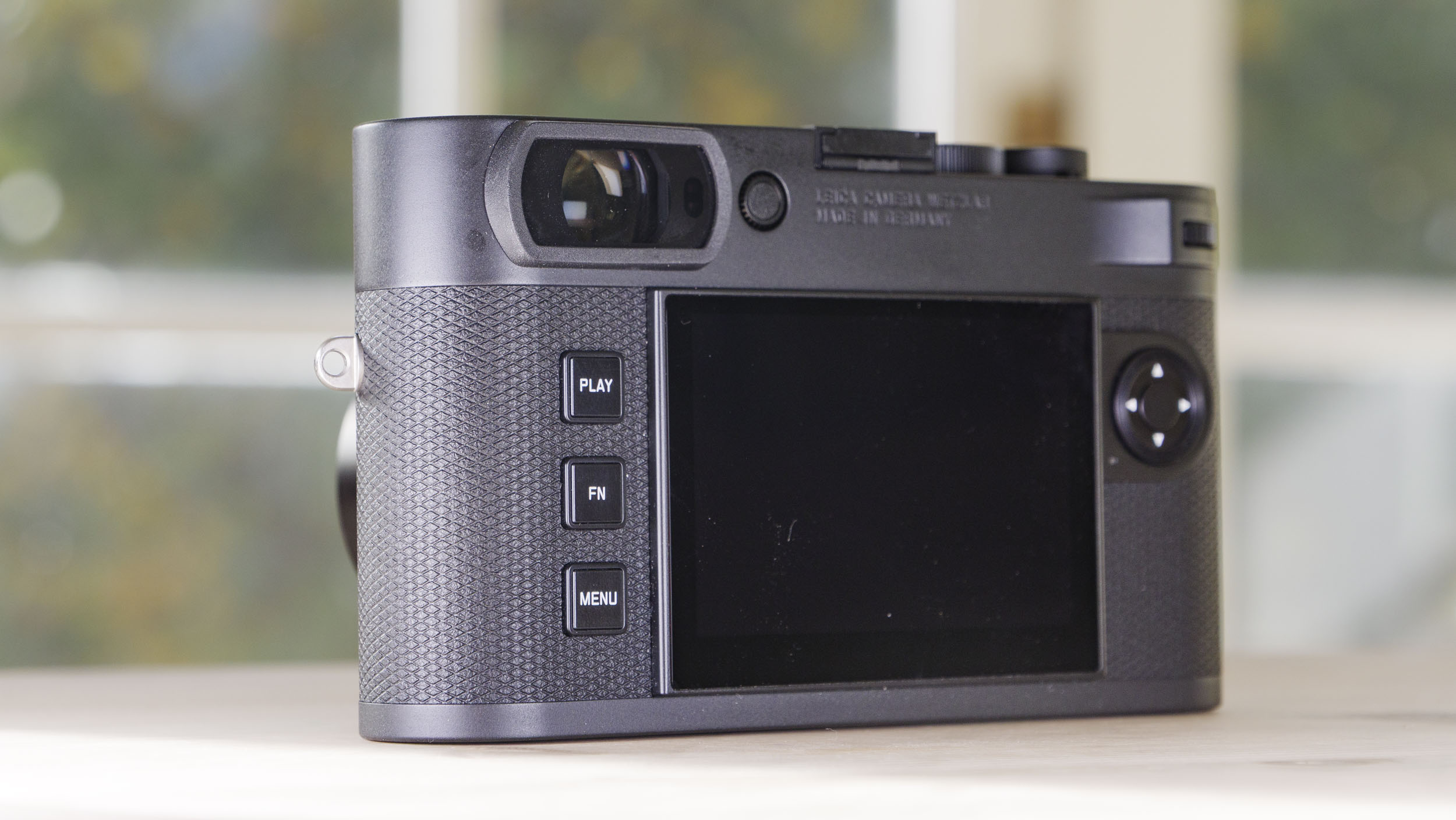 Rear of the Leica M EV1 camera, on a wooden table with glass-panelled door backdrop