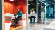 A photo of three businesspeople in a modern workplace, with one on a tablet, another on a laptop, and a third on a phone.