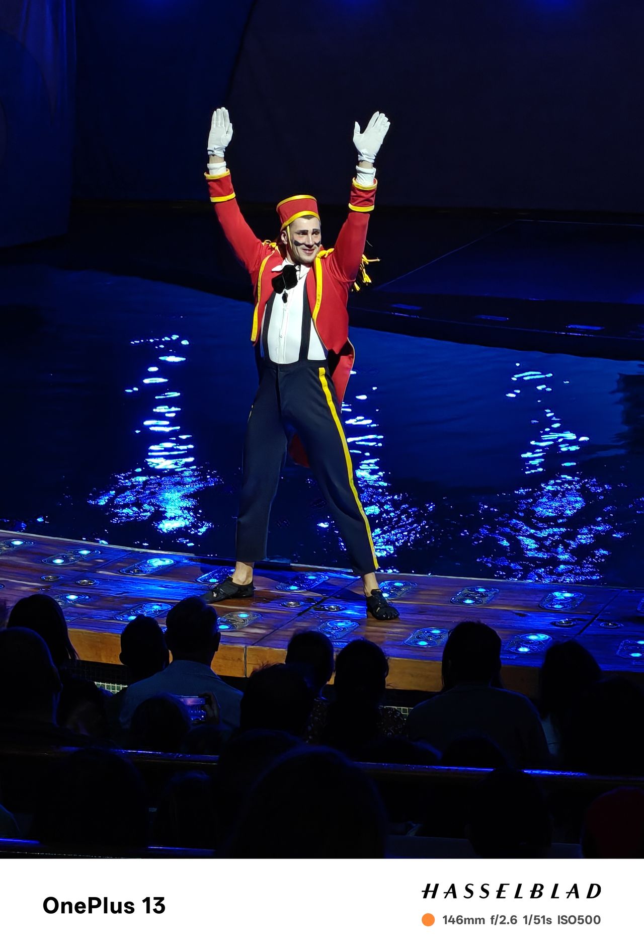 A person performing in circus outfit in front of a pool of blue-lit water