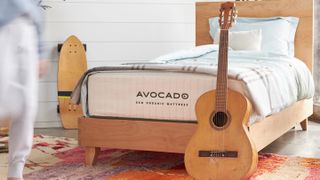 The Avocado Eco Organic Mattress placed on a wooden bed frame with an acoustic guitar