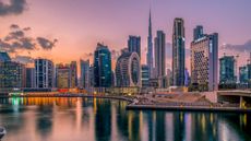 The Dubai skyline lights up at dusk on a partly cloudy evening