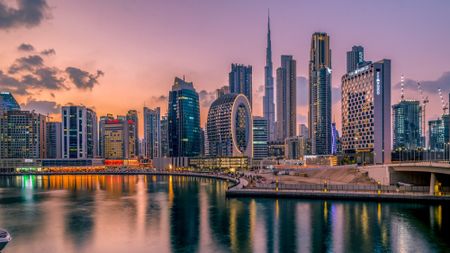 The Dubai skyline lights up at dusk on a partly cloudy evening