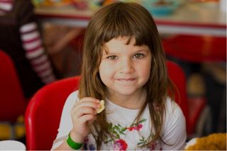 Child holding a crisp and looking at the lens