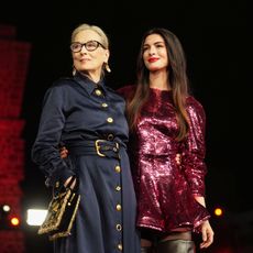 a woman in glasses in a blue jumpsuit next to a brunette woman in a red sparkly dress