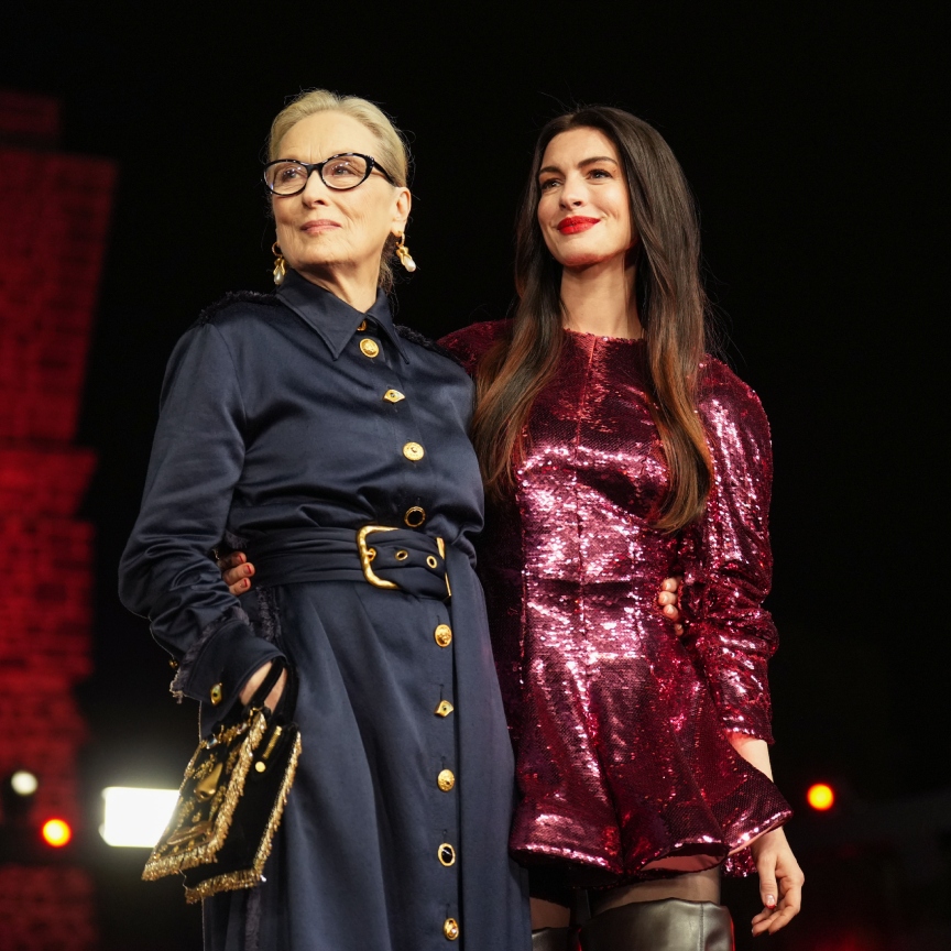 a woman in glasses in a blue jumpsuit next to a brunette woman in a red sparkly dress