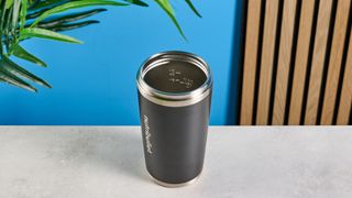 the Nutribullet Flip with a black insulated tumbler and a portable battery-powered blade photographed with a blue background. The tumbler has a carry strap and a sippy lid you can interchange, and an on/off button on the base.