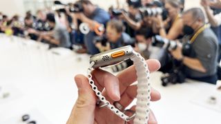 En hand som håller upp en Apple Watch Ultra med ett vitt armband, sett från sidan.
