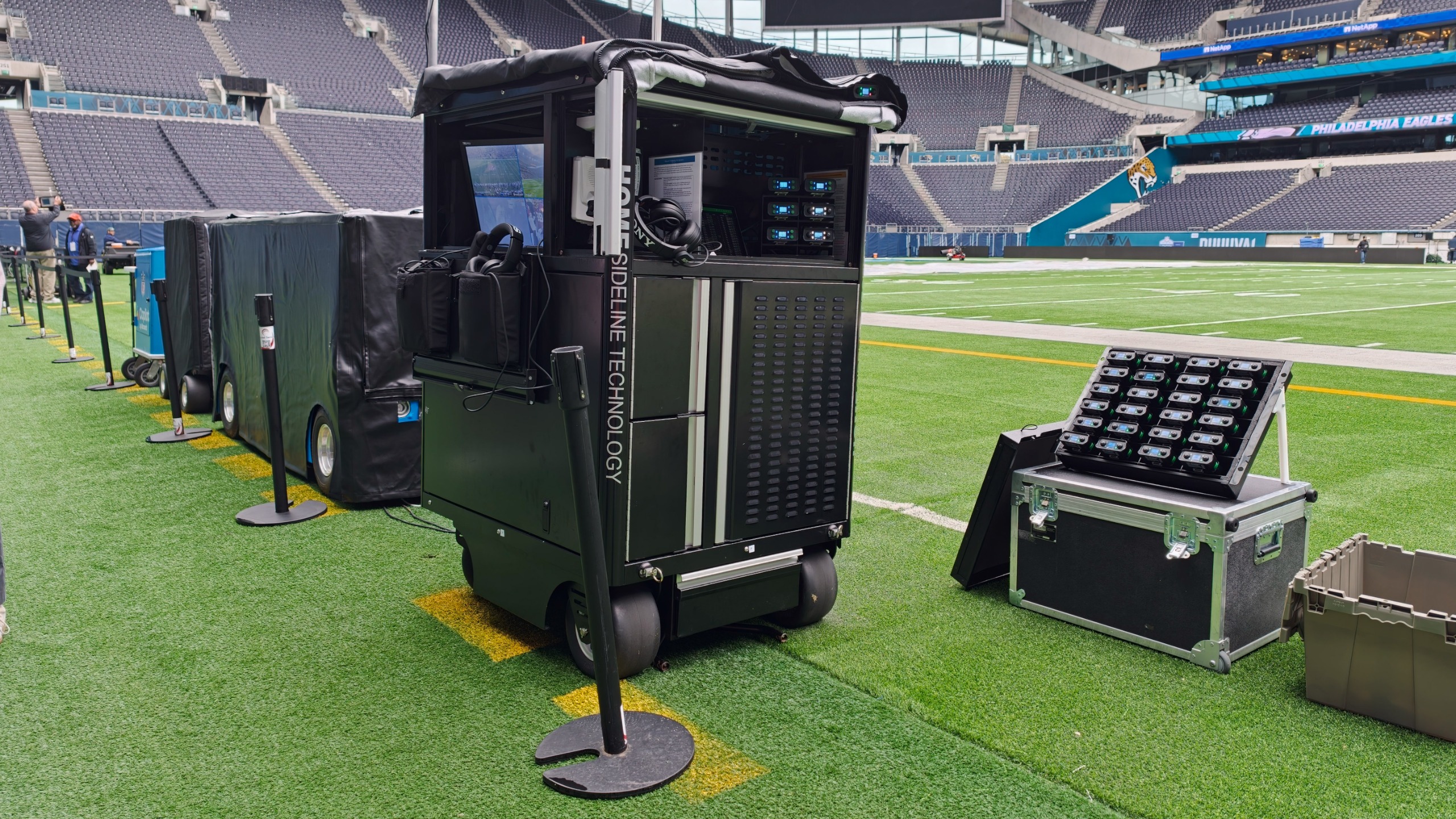 NFL sideline technology cart and equipment rack positioned beside the field inside a large stadium.