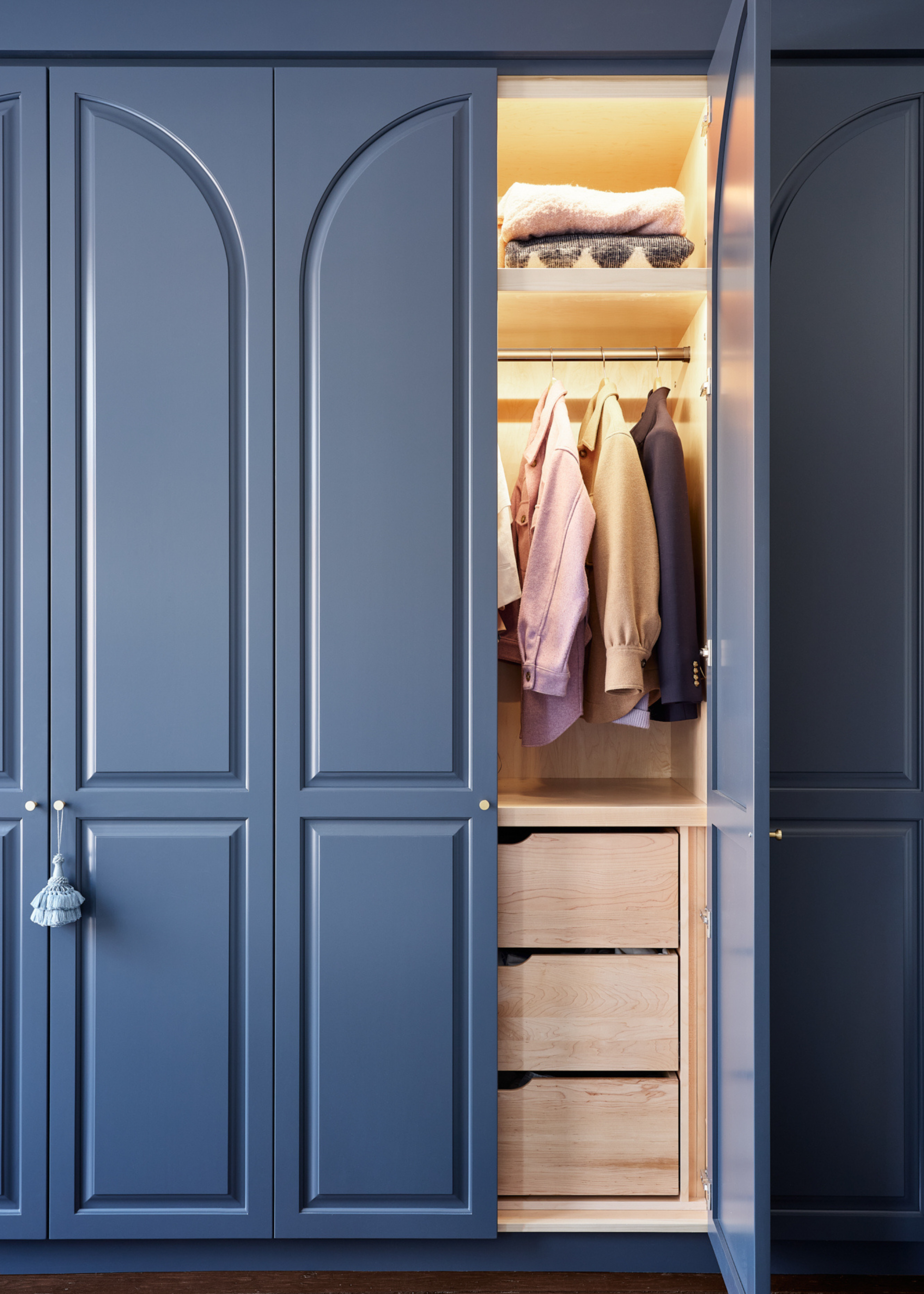 A blue clothes closet with cabinet lighting, wooden shelving, a clothes rod and sliding drawers