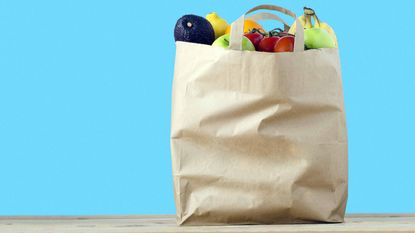 grocery bag full of fruits and vegetables in front of blue background