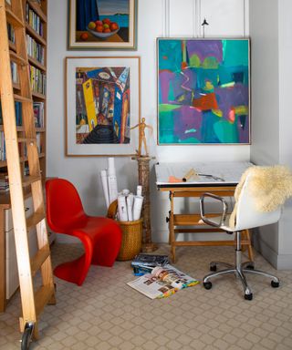Eclectic gallery wall with small person wooden sculpture on small desk, atop a lightly-patterned-wall-to-wall-carpet