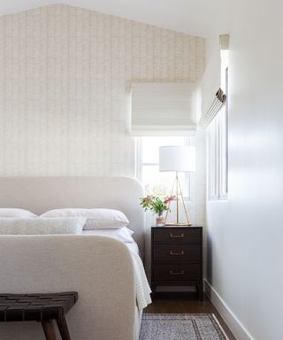 bedroom with sloping roof pale wallcovering and white upholstered bed with dark bedside cabinets