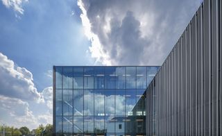 Daytime, exterior view of Cacao Factory, Helmond, glass panelled walls, strobe lighting inside, trees and surrounding area, blue cloudy sky