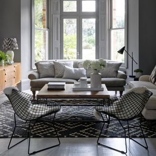 Grey lounge with grey sofa, chairs and patterned carpet next to wooden console