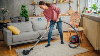 Young woman vacuuming rug