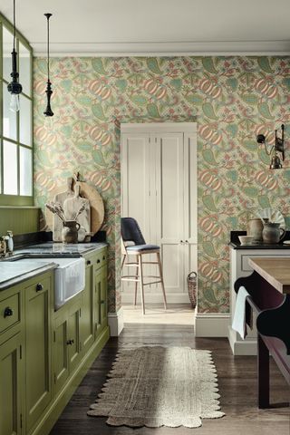 An example of how to make a small kitchen look bigger showing a kitchen with green floral wallpaper and green kitchen cabinets with a rug on the floor