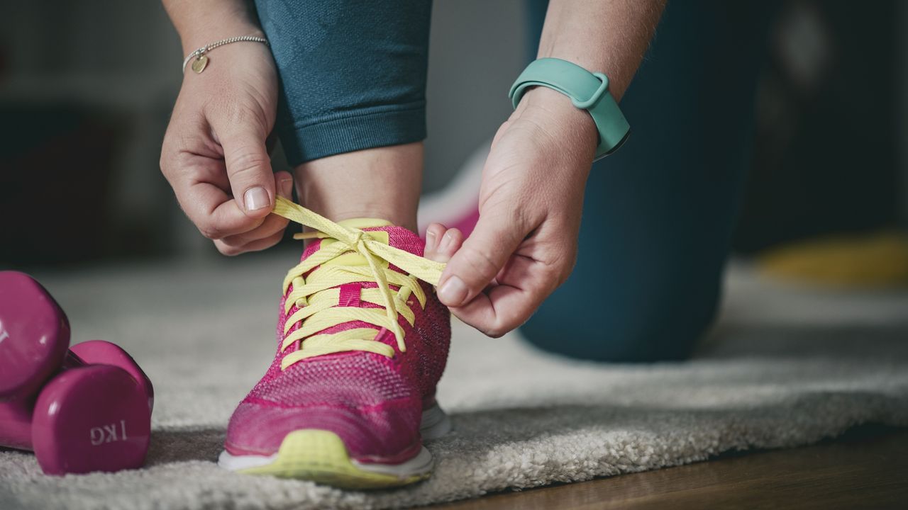 A woman ties the laces on her sneakers, getting ready for a workout.