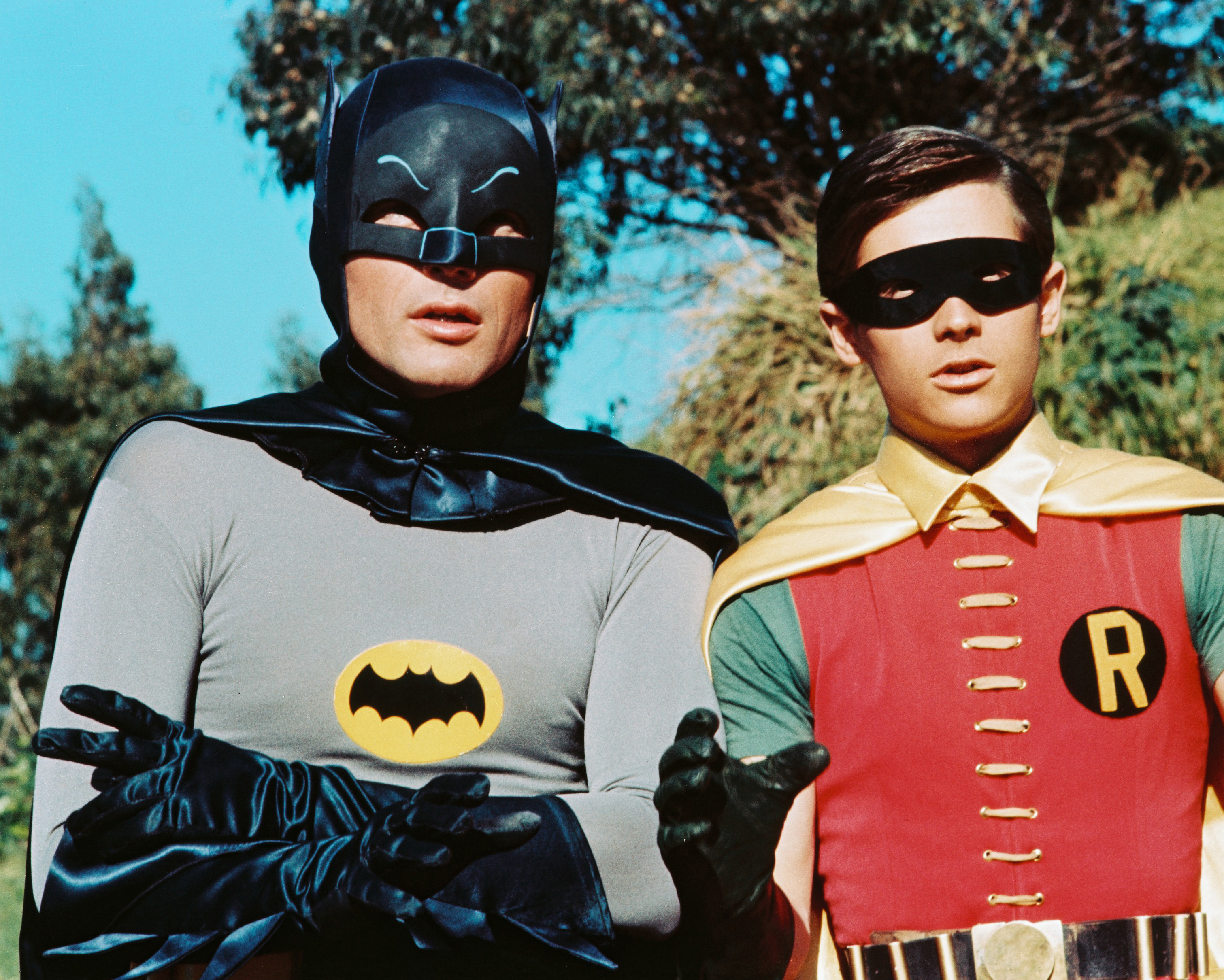 Batman and Robin in costume with trees and blue sky in the background