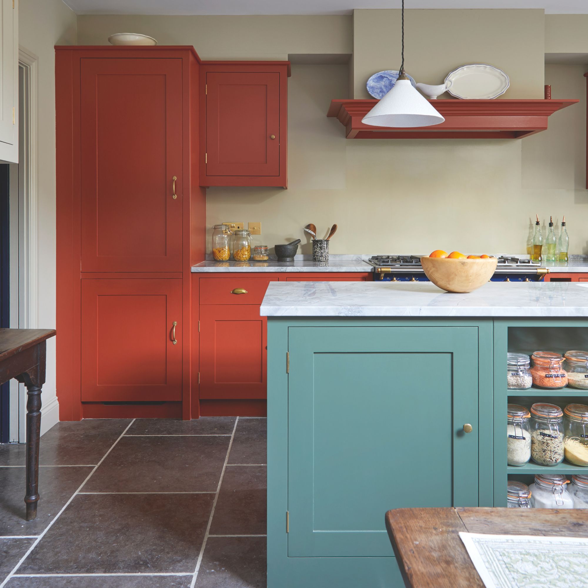 Beige painted kitchen with red cabinets on the back wall and an island with blue cabinets and a marble worktop