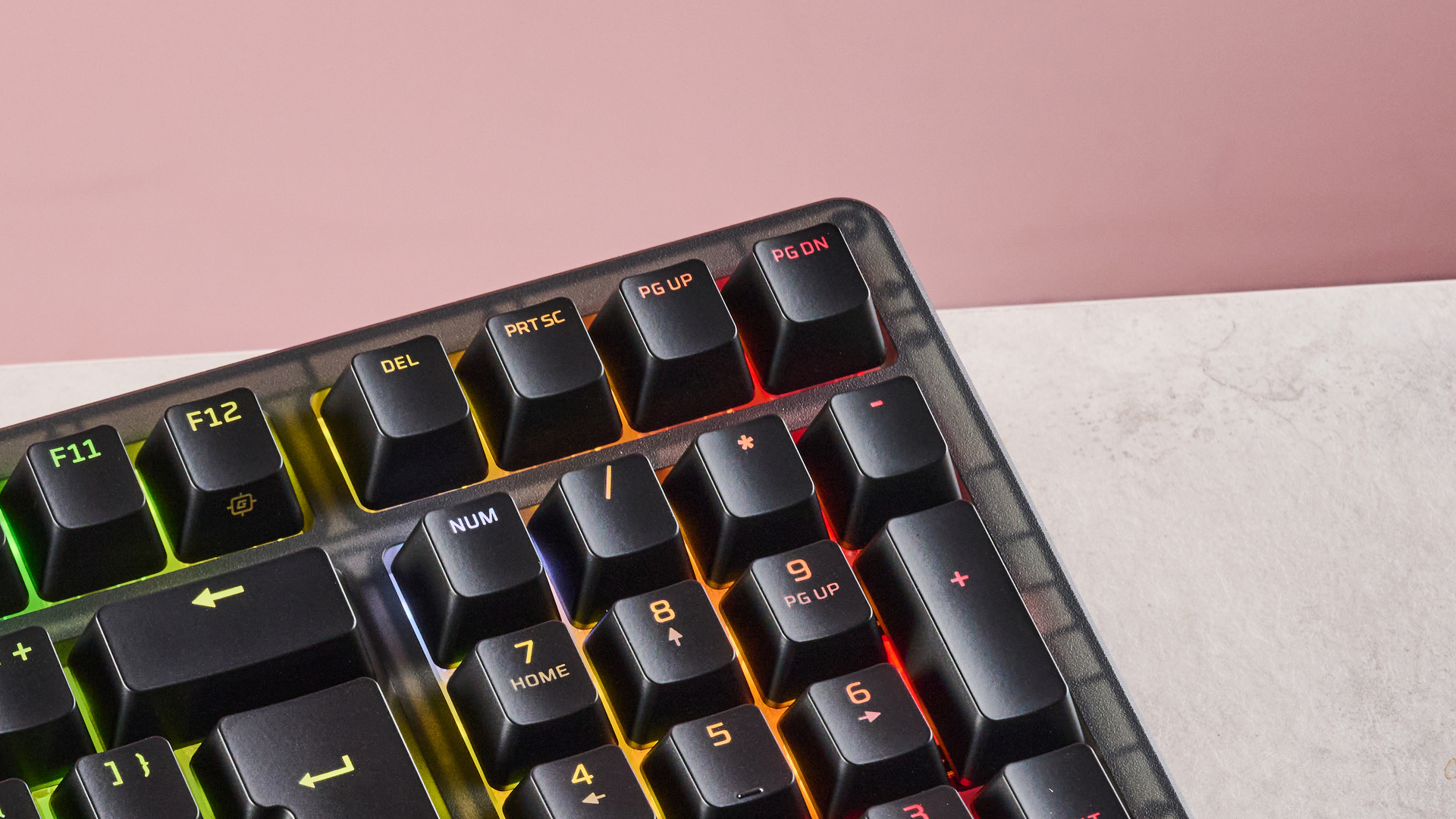 Close-up of top-right corner of HyperX Origins 2 1800, with RGB backlighting on, on a desk with pink wall in background
