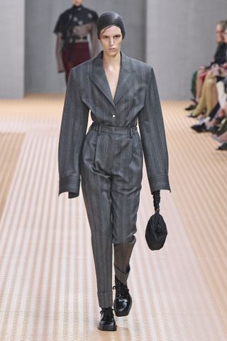 Prada model wearing a gray blazer and high-waisted pants on the SS24 runway.