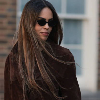 Woman styling her long hair with sunglasses and a brown jacket