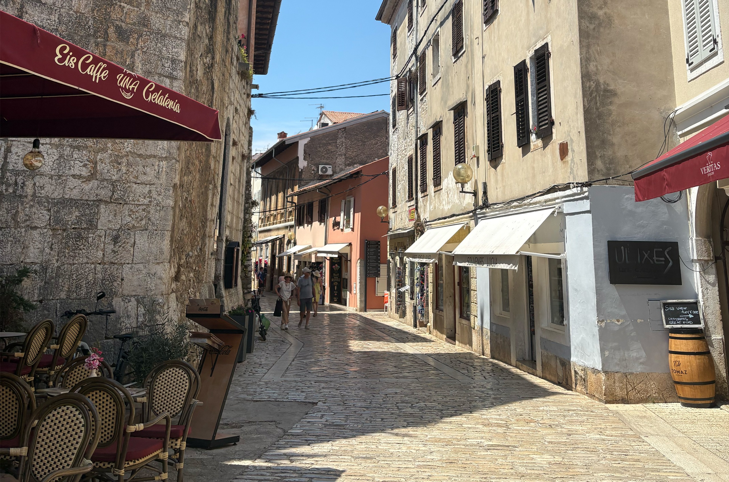 A cobbled street in Porec, with a cafe with outdoor seating on the left