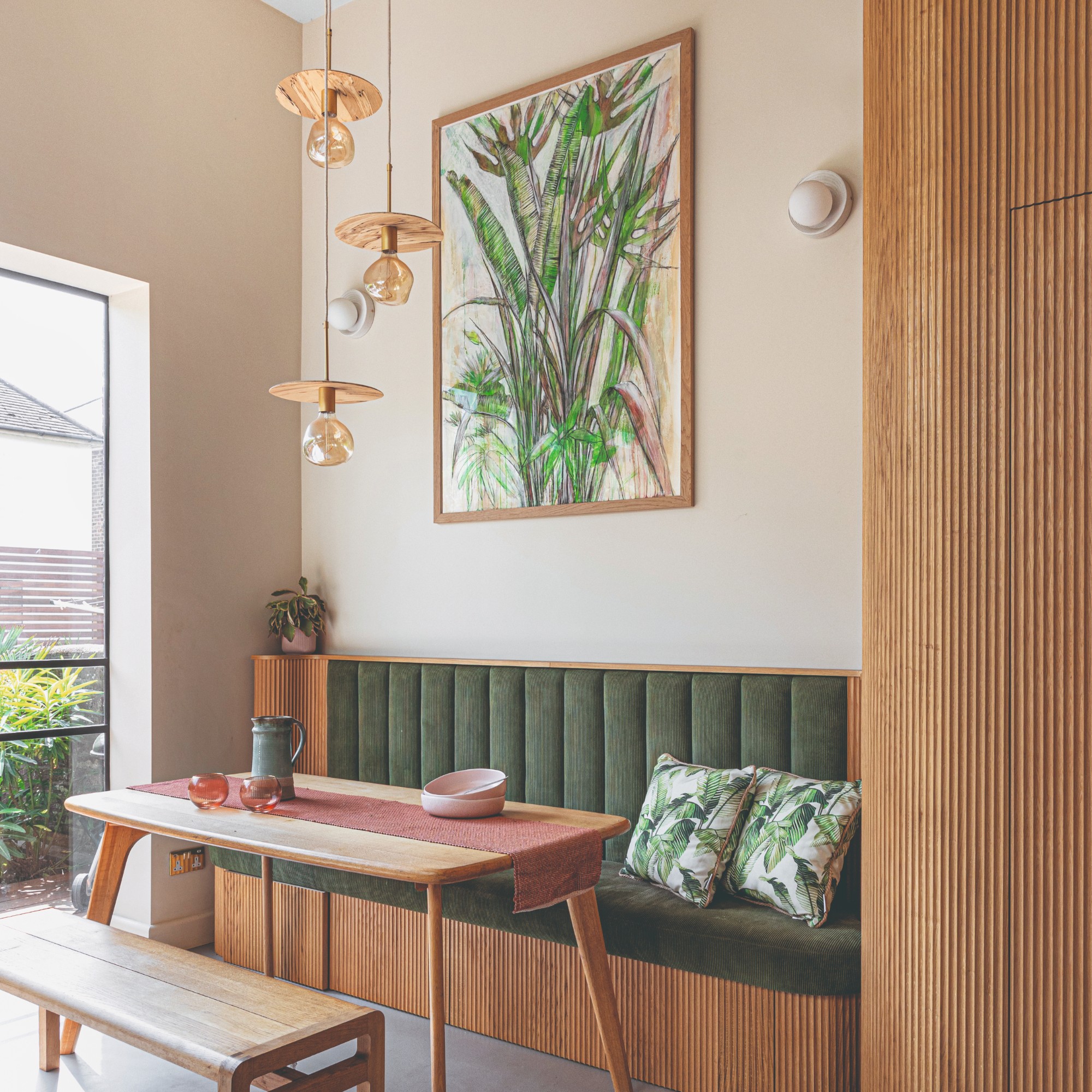 A dining nook with a built-in dining bench and another freestanding one with three pendant ceiling lights hanging above the table and two wall lights above it