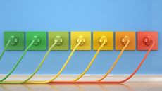 Blue wall and white baseboard with seven colorful plug sockets and matching wires. Left to right is three shades of green into two yellow then orange and red like a rainbow