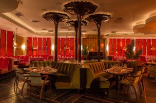 A Great Gatsby-inspired restaurant features plush velvety furniture in green, red, and orange tones, along with spectacular sculptural decorations scattered throughout.