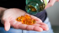 A close-up image of a person pouring yellow pills onto their hand out of a green-tinged bottle. 