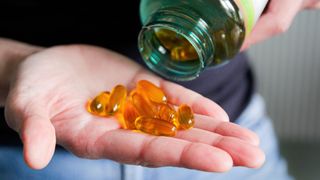 A close-up image of a person pouring yellow pills onto their hand out of a green-tinged bottle. 