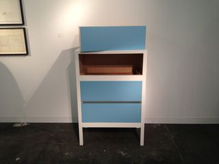 A piece of storage furniture with three light blue drawers with one drawer removed and resting on the top.