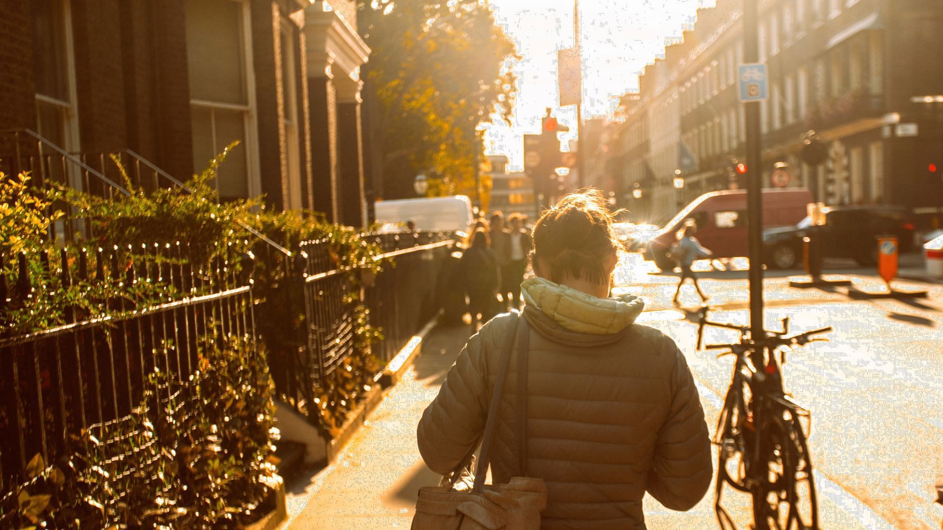 A woman walks along a city street in the evening sunlight.