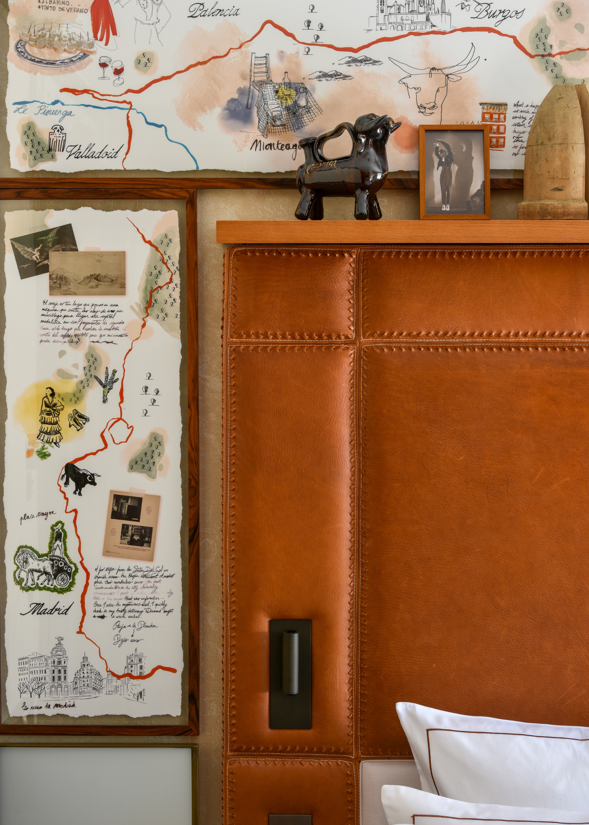 A leather headboard with a top shelf of ceramic and decor backed by a map with pictures and illustrations