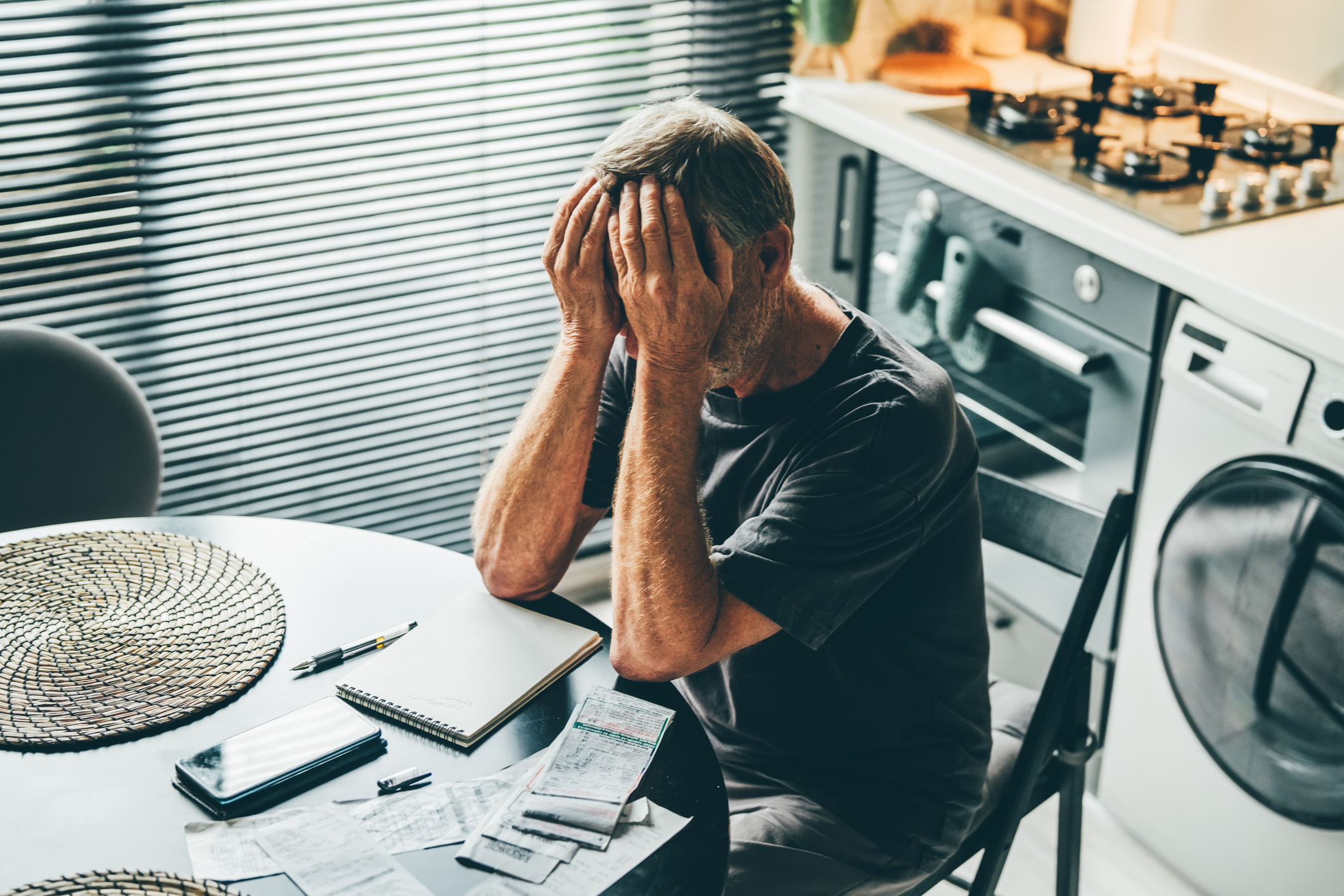 State pensioner holding his head in his hands worried about money