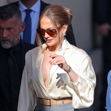 Jennifer Lopez wearing a white satin button-down blouse with wide-leg trousers and platform shoes, arriving at Jimmy Kimmel Live in Los Angeles