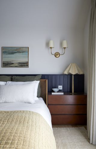 A bedroom with wooden chest of drawers and bed with white pillows
