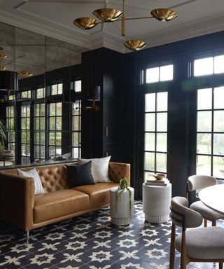 living and dining space with black and white tiled floor, tan leather couch, brass pendant lights, black walls, mirror