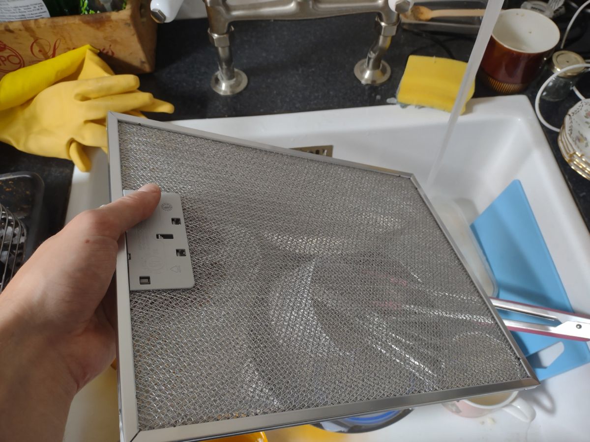 The metal mesh from a cooker hood extractor fan being washed in a kitchen sink