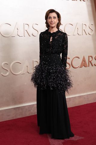 A photo of Fernanda Torres wearing a long-sleeved black Chanel dress adorned with lace and feathers.