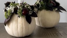 two white pumpkins with dark flowers adorning them