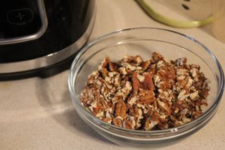 A bowl of chopped pecans next to the Oster 10-Cup Food Processor with Easy-Touch
