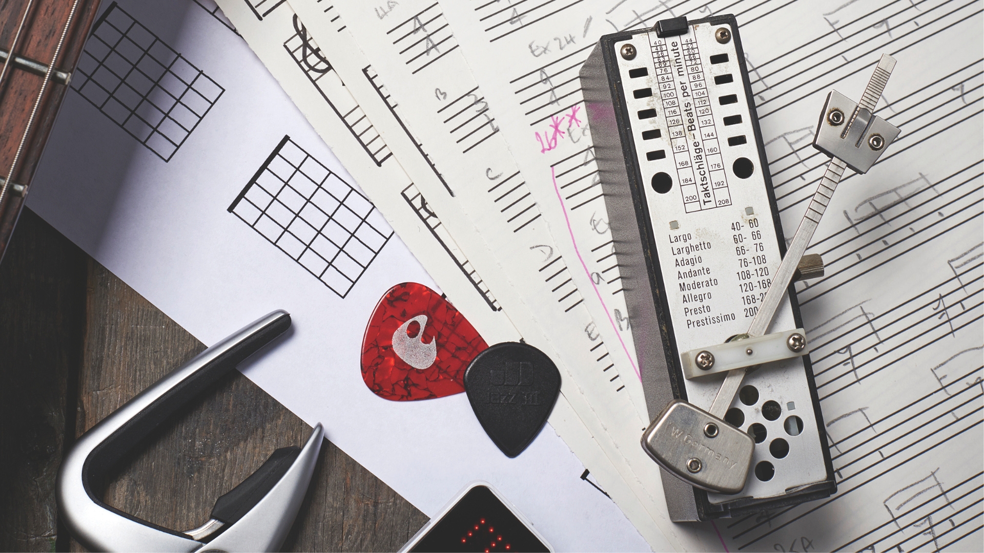 A metronome lying on sheet music with guitar picks and a capo in the background
