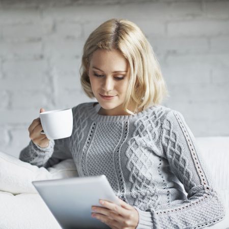 Woman looking at a tablet computer while holding a coffee cup.